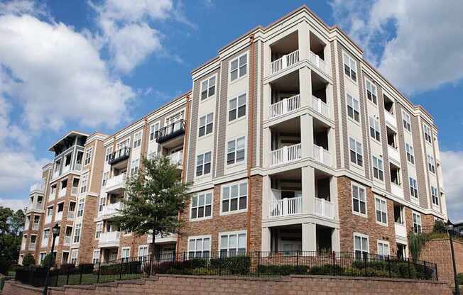 A large apartment building with balconies and a brick wall in front.