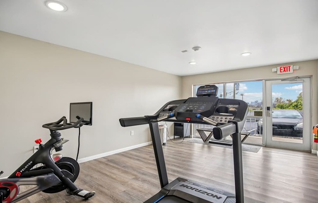 A treadmill and a stationary bike are in a room with a window.
