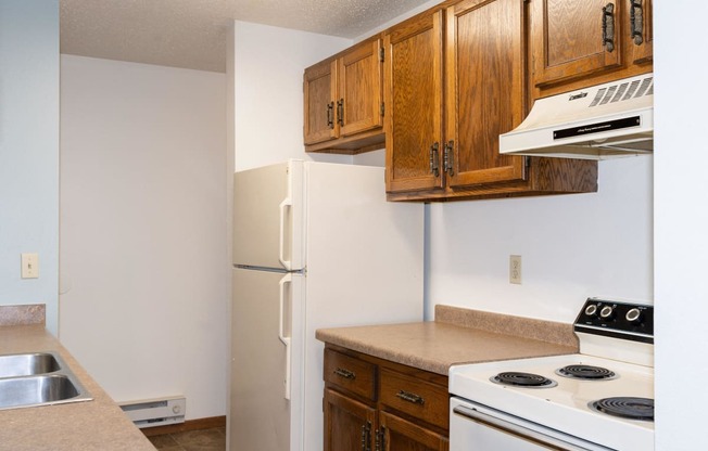 a kitchen with white appliances and wooden cabinets and a refrigerator. Fargo, ND Pacific South Apartments