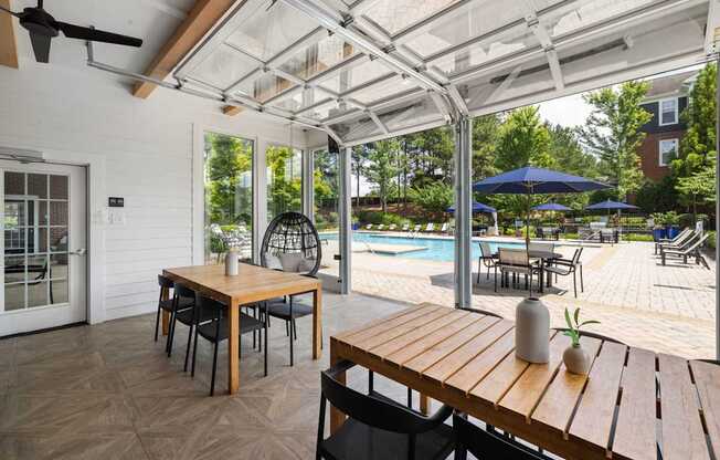 A garage with tables, chairs, and a kitchen that opens up to the pool