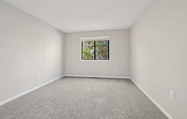 A bedroom with a window and carpeted floor.
