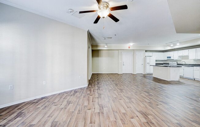 an empty living room with a ceiling fan and a kitchen