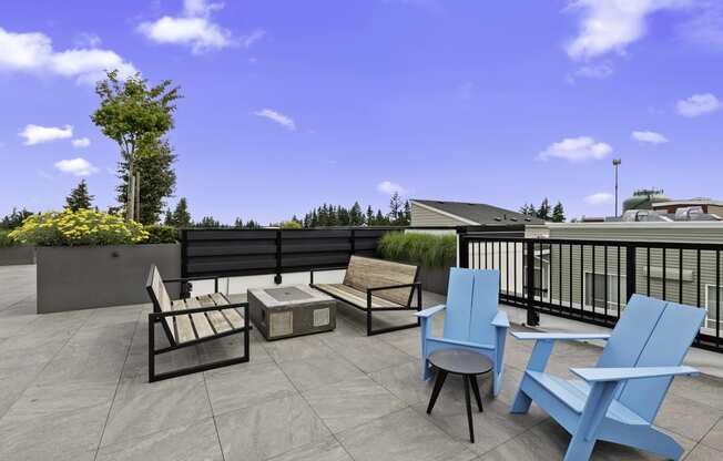 Two Blue Adirondack Chairs with two wooden benches facing cozy fireplace on the Resident Rooftop Lounge with a blue sky in the background at Arabella Apartment Homes, Shoreline, Washington 98155