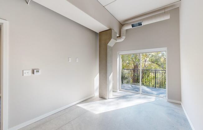 an empty living room with a sliding glass door to a balcony