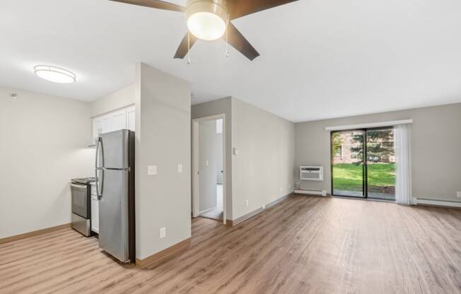 an empty living room with a refrigerator and a ceiling fan