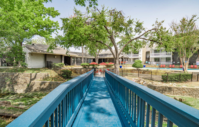 a blue bridge over a swimming pool with houses in the background