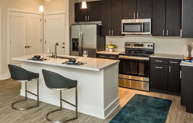 A modern kitchen with a white island and black chairs.