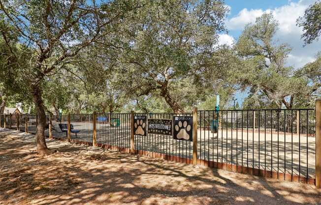 a park with trees and a fence with signs on it