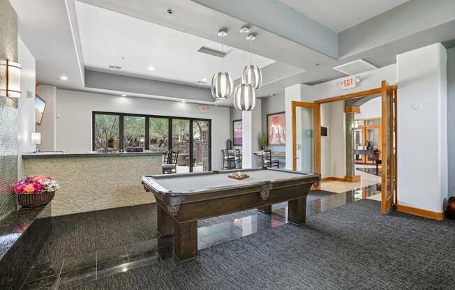 A pool table is in the middle of a room with a bar and a door.