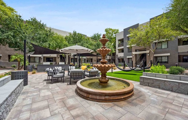 a fountain in the middle of a patio with chairs and umbrellas