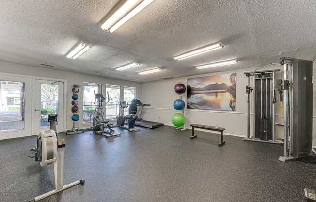 A gym with a variety of equipment including a stationary bike, a treadmill, a rowing machine, a bench, and a wall with a poster.