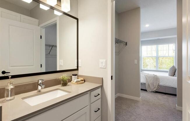 A bathroom with a sink, mirror, and a bedroom in the background.