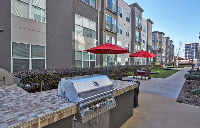 an outdoor kitchen with a grill and umbrellas in front of an apartment building at Mockingbird Flats, Texas