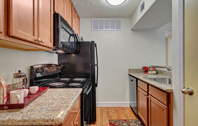 A bright kitchen at Acacia Park with warm wood cabinetry, granite-style countertops, modern black appliances, and efficient overhead lighting that creates a practical and inviting cooking space.