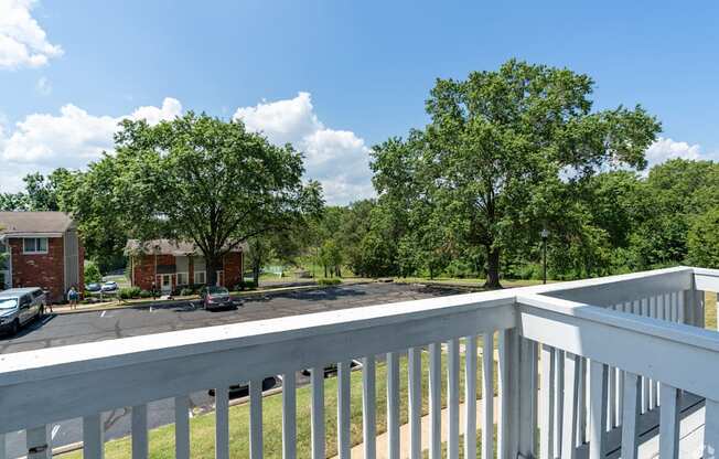 A white railing overlooks a grassy area with trees and a building in the distance.
