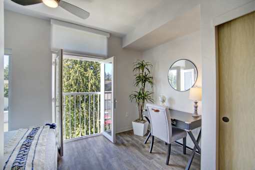 A bedroom with a bed, desk, chair, and a balcony with a view of trees.