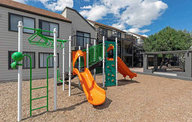 A playground with a green ladder, a green and orange slide, and a green and orange climbing structure.