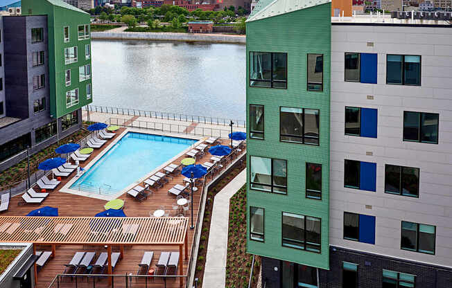 A green building with a pool in the foreground and a city skyline in the background.