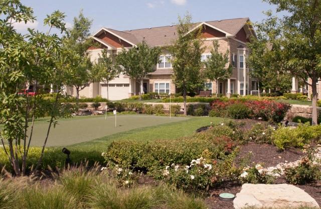Meticulously maintained grounds with mature trees surround the soft tan paint and brick exterior apartment homes at Villas at Carrington Square Apartments, Overland Park, KS 66221