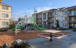 A playground with a green slide and a picnic table in front of apartment buildings. at Mill Creek Meadows Apartments, Mill Creek