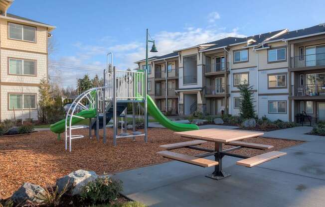 A playground with a green slide and a picnic table in front of apartment buildings. at Mill Creek Meadows Apartments, Mill Creek