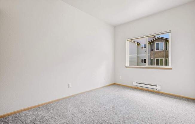 A bedroom with a carpeted floor and a window showing the apartment complex outside at The Madison Apartments in Olympia, WA