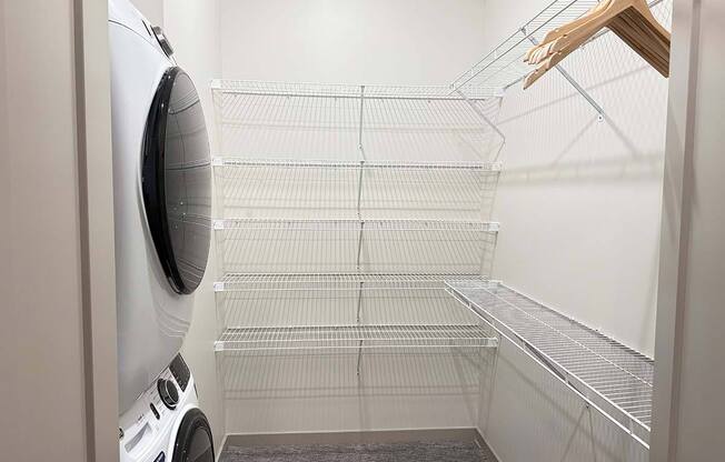 a walk-in closet with built-in shelving and hanging space and a stackable washer and dryer in it