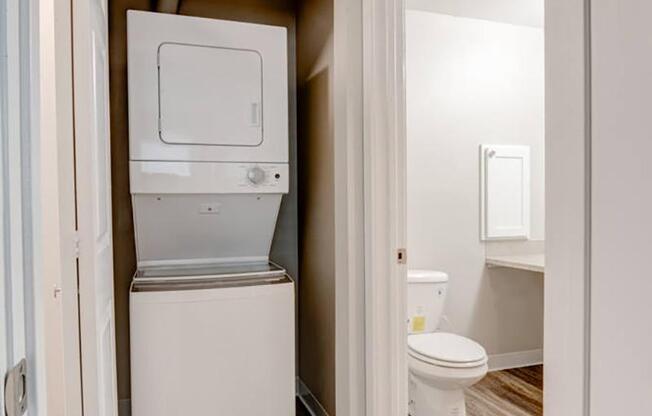 A laundry closet with a white stacked washer and dryer and a door to the bathroom on the right.