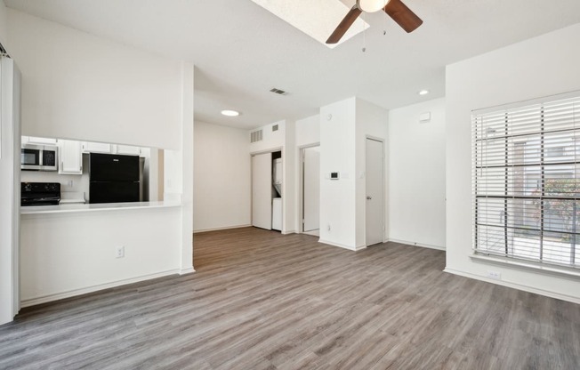 an empty living room with a ceiling fan and a kitchen