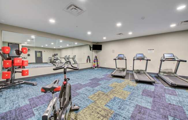 a gym with cardio machines and large mirrors at The Vue apartments