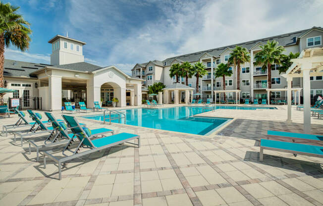 a swimming pool with chaise lounge chairs and a building in the background