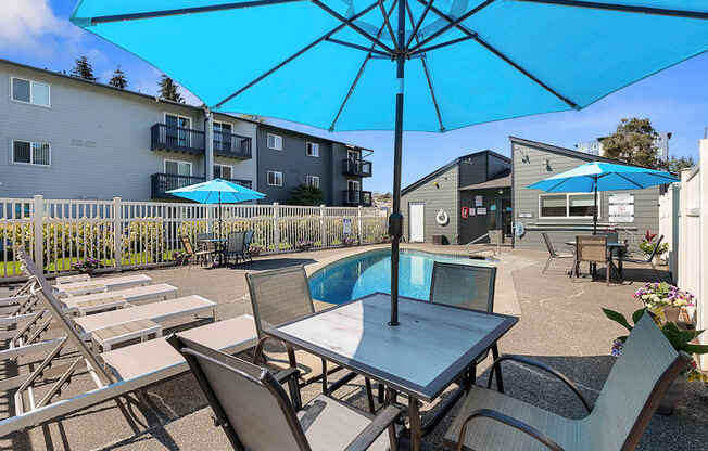 a patio with a pool and chairs and umbrellas at Pacific Park Apartment Homes, WA 98026