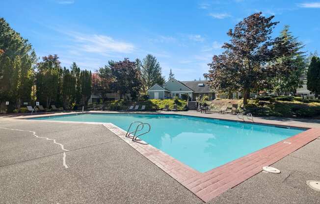 A large outdoor swimming pool surrounded by trees and a building in the background at Clackamas Trails Apartments, Oregon, 97222