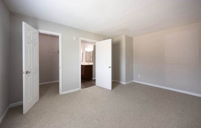 A room with carpeted floors and white walls with three open doors.