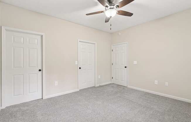 A room with a ceiling fan and three doors.