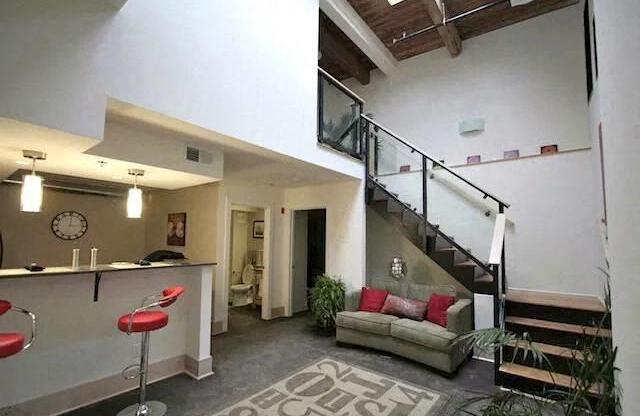 a room with a staircase and a living room with red chairs