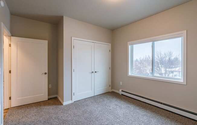 an empty bedroom with two doors and a window. Fargo, ND Prairiewood Meadows Apartments