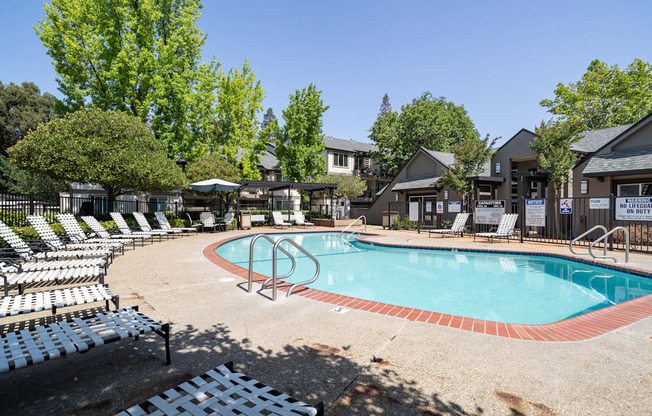 A pool surrounded by chairs and trees.