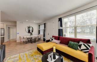 Living room with red and yellow couch and Harwood inspired flooring. Dining area in the distance at Morgan Ranch Apartments, Morgan Hill, CA