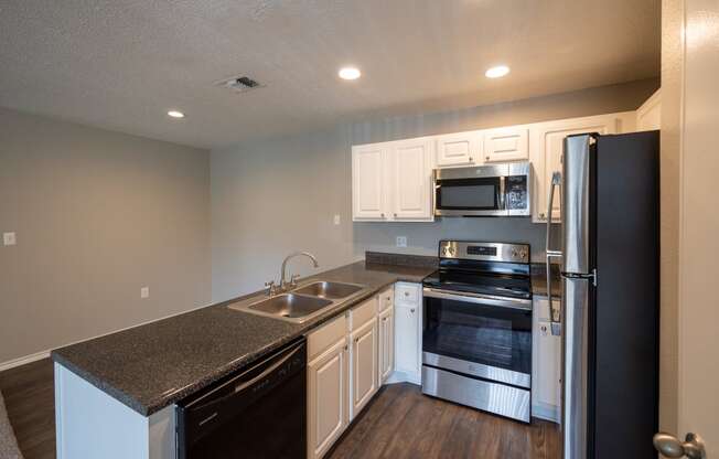 View of open kitchen and dining with dark counters, stainless and black appliances, white cabinets, and wood look flooring