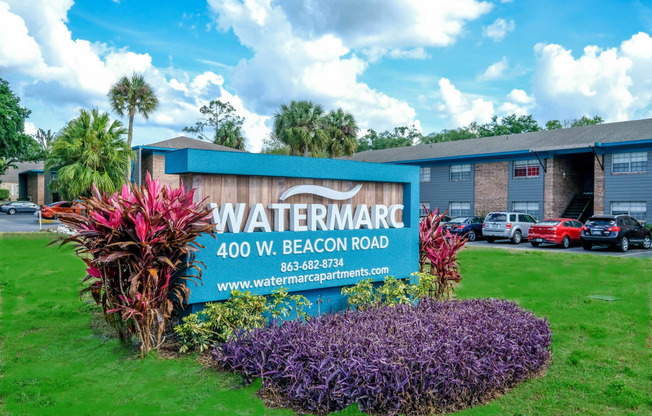 Blue concrete Monument sign in lakeland, FL, that reads "Watermark - 400 W Beacon Road" surrounded by pink and purple tropical flowers.