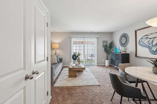 A living room with a grey couch, a wooden coffee table, a white door, a white wall, a television, a plant, and a butterfly picture at Staples Mill Townhomes Apartments, Richmond 23228