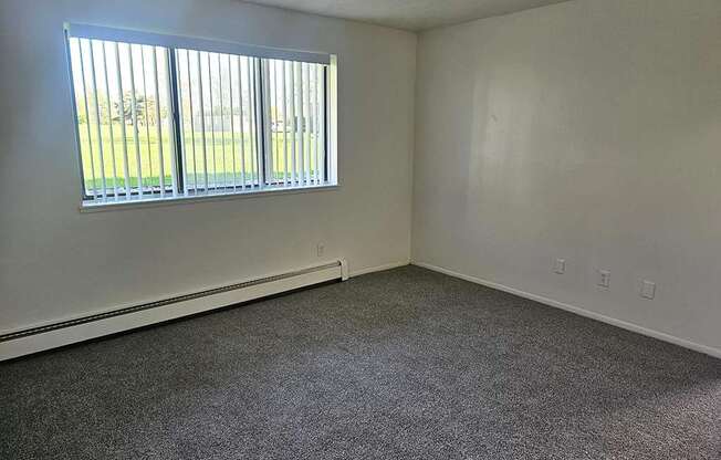 A living room with a carpeted floor and a window with blinds at Waverly Park Apartments, Lansing