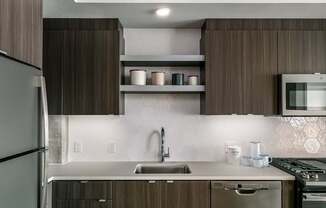 A modern kitchen with a refrigerator on the left and a microwave above the stove.