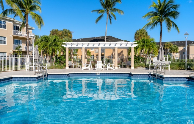 A pool with a white pergola and palm trees in the background.