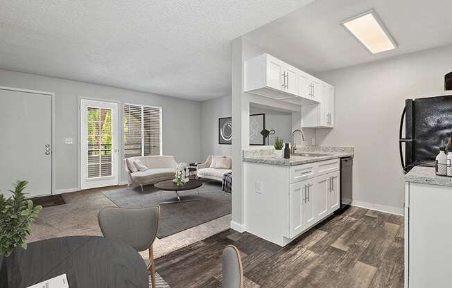 Model Kitchen with White Cabinets and Wood-Style Flooring with View of Dining/Living Room Area at Stillwater Apartments in Glendale, AZ.