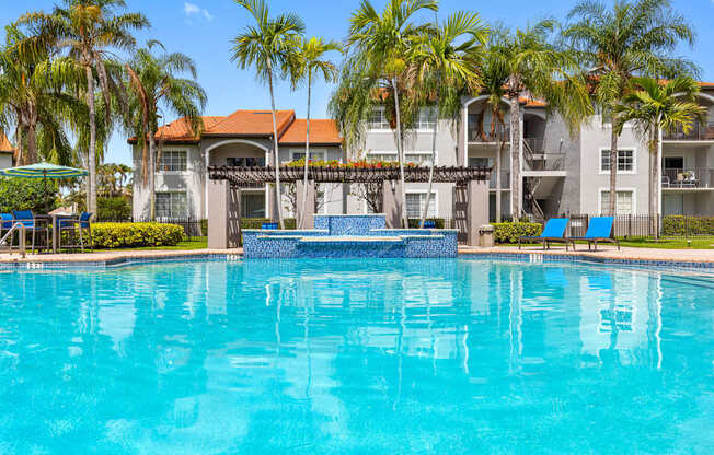 A swimming pool surrounded by palm trees and a building in the background.