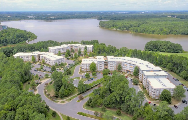 A large white building complex is surrounded by trees and a body of water.