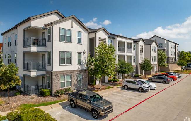 A row of apartment buildings with cars parked in front.