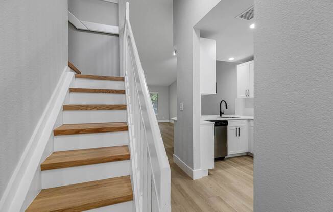 A staircase with wooden steps and white railings leads to a kitchen area.